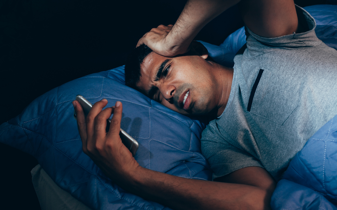 Sleeping man being woken up by mobile phone in bedroom at night