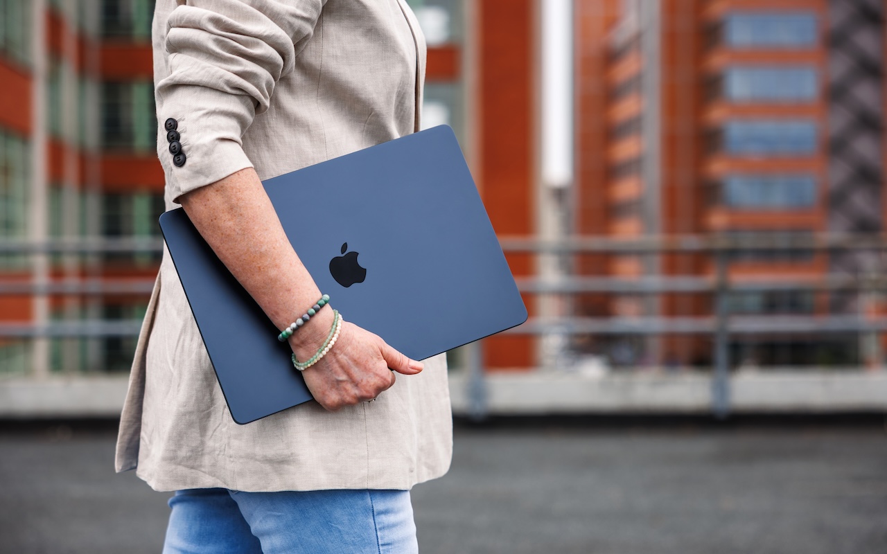 Woman with Apple laptop MacBook Air with M4 chip is walking outside of office building